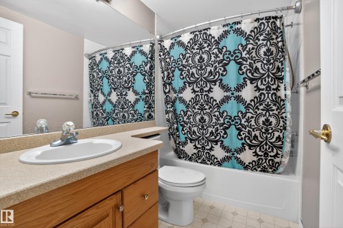 Bathroom featuring a wood-finish vanity with a built-in sink, a light-colored countertop, and a full-width mirror - 104 9760 174 Street, Edmonton, AB - Indoor Photo Showing Bathroom