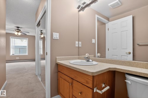 Bathroom vanity with a light-toned countertop, integrated sink, and wood-finish cabinetry - 104 9760 174 Street, Edmonton, AB - Indoor Photo Showing Bathroom