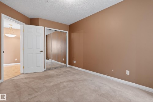 Carpeted room featuring a mirrored closet, a standard white door with dark hardware, and neutral-toned walls - 104 9760 174 Street, Edmonton, AB - Indoor Photo Showing Other Room