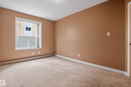 Carpeted room with a white-trimmed window, beige walls, and white baseboards - 104 9760 174 Street, Edmonton, AB - Indoor Photo Showing Other Room