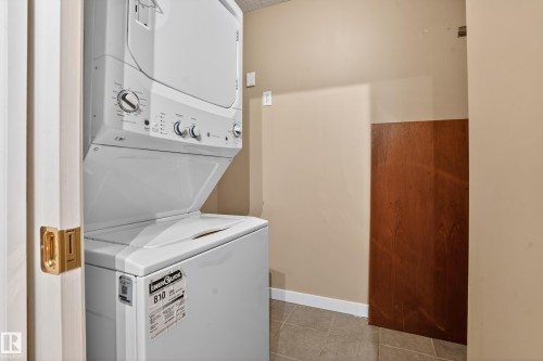 Dedicated laundry area featuring a stacked washer and dryer unit, neutral wall paint, white baseboards, and tile flooring - 104 9760 174 Street, Edmonton, AB - Indoor Photo Showing Laundry Room