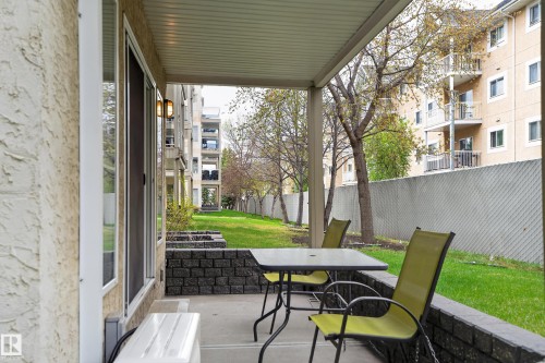 Covered concrete patio with stucco exterior, sliding glass door access, and a retaining wall featuring block stone - 104 9760 174 Street, Edmonton, AB - Outdoor With Exterior