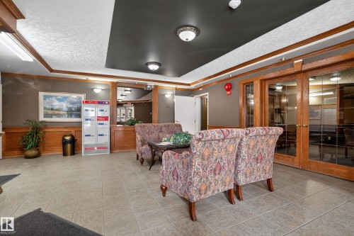 Lobby area featuring wood wainscoting, neutral tile flooring, and double glass doors - 104 9760 174 Street, Edmonton, AB - Indoor Photo Showing Other Room