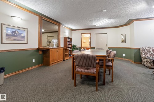Spacious common area featuring textured carpeting, chair rail molding with a two-tone wall finish, and flush-mount ceiling lighting - 104 9760 174 Street, Edmonton, AB - Indoor