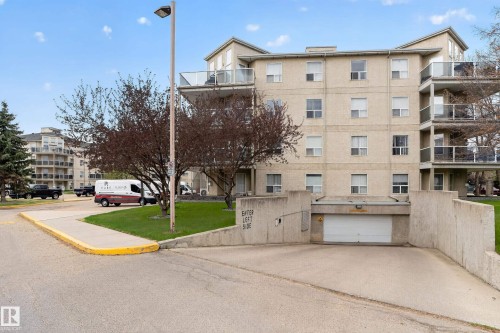 Multi-story building featuring a beige exterior, multiple private balconies with glass railings, and a ground-level garage entrance with a white door - 104 9760 174 Street, Edmonton, AB - Outdoor