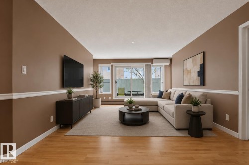 Spacious living area featuring wood-finish flooring, neutral wall tones with white trim, and a large sliding glass door with transom window - 104 9760 174 Street, Edmonton, AB - Indoor Photo Showing Living Room