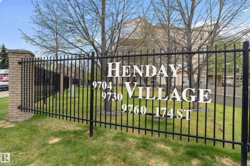 Black wrought iron fencing with a brick pillar, featuring "HENDAY VILLAGE" signage and property numbers - 104 9760 174 Street, Edmonton, AB - Outdoor
