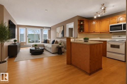 Open-concept living space featuring wood-finish flooring, a kitchen with wood cabinetry and countertop, and a living area with sliding glass doors opening to the patio - 104 9760 174 Street, Edmonton, AB - Indoor