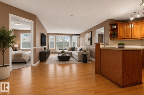 Open-concept living space featuring wood-finish flooring, a kitchen with wood cabinetry and countertop, and a living area with sliding glass doors - 104 9760 174 Street, Edmonton, AB - Indoor Photo Showing Other Room