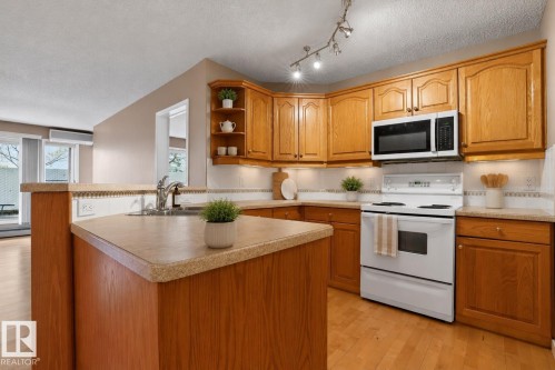 Kitchen featuring wood cabinetry, white appliances, track lighting, and wood-finish flooring - 104 9760 174 Street, Edmonton, AB - Indoor Photo Showing Kitchen