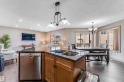 The kitchen features wood cabinetry, a double sink, and a stainless steel dishwasher - 