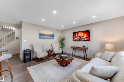 The living area features recessed lighting, durable wood-look flooring, and a staircase with light-colored banisters - 