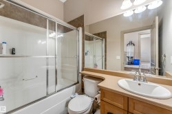 Bathroom featuring a white bathtub with a sliding glass door, a toilet, and a vanity with an oval sink and chrome faucet - 