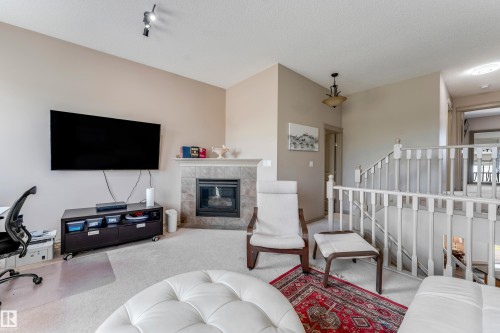 Living area featuring a fireplace with a tiled surround, light-colored carpet, and a white balustrade - 463 Tamarack Green, Edmonton, AB - Indoor Photo Showing Other Room With Fireplace