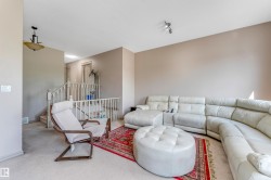Living area featuring light-colored walls, carpeted floors, and a stairway with white railings - 