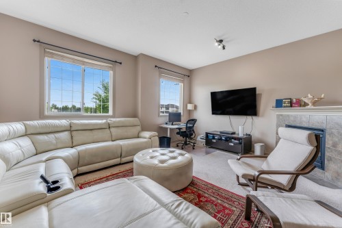 This inviting living area features neutral-toned walls, windows providing natural light, and a fireplace with a tiled surround - 463 Tamarack Green, Edmonton, AB - Indoor Photo Showing Living Room With Fireplace