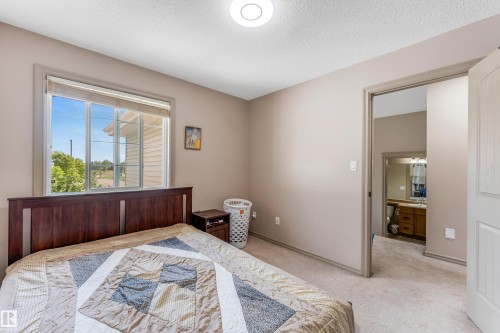 This bedroom features a window with blinds, carpeted flooring, and direct access to a bathroom - 463 Tamarack Green, Edmonton, AB - Indoor Photo Showing Bedroom