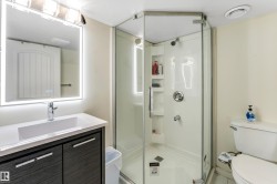 The bathroom features a vanity with a rectangular sink, a back-lit mirror, and a glass-enclosed shower - 