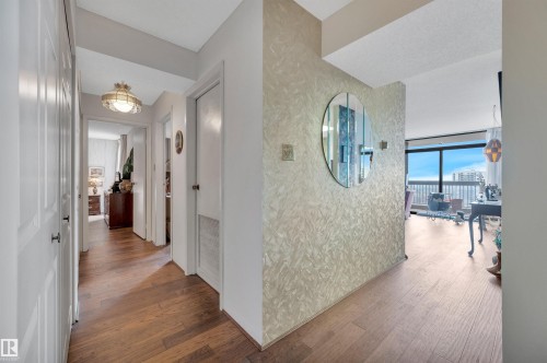 Entryway featuring wood-finish flooring, a decorative wall with a circular mirror, and a clear line of sight to expansive windows - 1603 10025 113 Street, Edmonton, AB - Indoor Photo Showing Other Room
