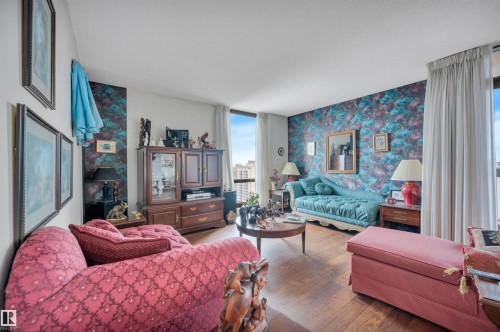Living area with wood-finish flooring, full-height windows, patterned accent wall, and white ceiling - 1603 10025 113 Street, Edmonton, AB - Indoor Photo Showing Living Room