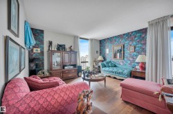 Living area with wood-finish flooring, full-height windows, patterned accent wall, and white ceiling - 
