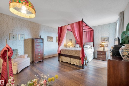 Spacious bedroom featuring wood-finish flooring, patterned wallpaper, a decorative ceiling light fixture, and window with drapes - 1603 10025 113 Street, Edmonton, AB - Indoor Photo Showing Bedroom