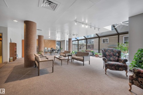 Carpeted common area featuring multiple seating arrangements, columnar architectural elements, a dining space, and an expansive glass enclosure providing natural light - 1603 10025 113 Street, Edmonton, AB - Indoor Photo Showing Other Room