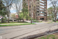 Multi-story brick facade building featuring a formal entryway, multiple balconies, mature trees, and a concrete parking structure - 