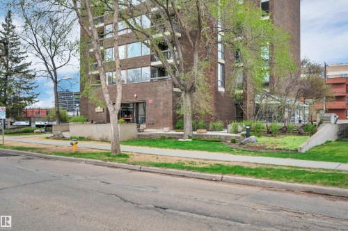 Brick building facade with multiple windows, concrete planters, and established landscaping - 1603 10025 113 Street, Edmonton, AB - Outdoor