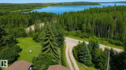 Expansive property featuring a vibrant green lawn, mature evergreen trees, and a gravel driveway - 