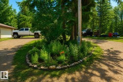 Gravel driveway with a central landscaped island featuring a stone border, verdant plantings, and mature trees - 