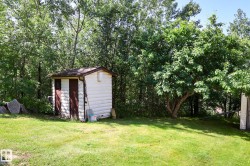Detached utility shed with painted wooden siding and two brown doors, positioned on a grassy lawn - 