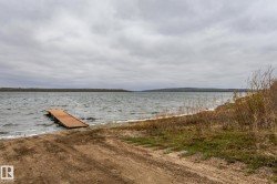 Waterfront property featuring a wooden dock extending into the water, a sandy shoreline, and distant tree-lined hills - 