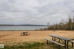 Sandy shoreline featuring a vast body of water, distant tree-lined hills, and multiple wooden picnic tables - 
