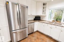 Kitchen featuring white shaker-style cabinetry, stainless steel appliances, a double basin sink, stone-finish countertops, and wood-finish flooring - 