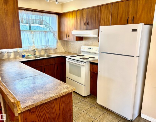 The kitchen features a double basin stainless steel sink, a stove with a range hood, and a refrigerator - 15208 92 Street, Edmonton, AB - Indoor Photo Showing Kitchen With Double Sink