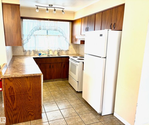 The kitchen features wood cabinetry, a double basin sink, and tile flooring - 15208 92 Street, Edmonton, AB - Indoor Photo Showing Kitchen With Double Sink