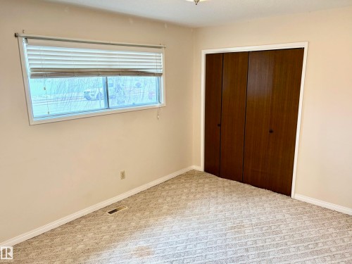 This room features neutral-toned walls, patterned carpeting, a window with horizontal blinds, and a closet with bifold doors - 15208 92 Street, Edmonton, AB - Indoor Photo Showing Other Room