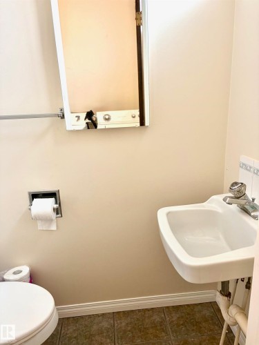 The bathroom features a wall-mounted sink with a chrome faucet, a white toilet, and tiled flooring - 15208 92 Street, Edmonton, AB - Indoor Photo Showing Bathroom