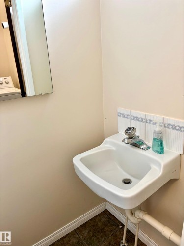 The property features a wall-mounted sink with a chrome faucet, complemented by a tiled backsplash - 15208 92 Street, Edmonton, AB - Indoor Photo Showing Bathroom