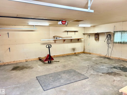 The property features a garage with concrete flooring, overhead lighting, and wall-mounted shelving - 15208 92 Street, Edmonton, AB - Indoor Photo Showing Garage