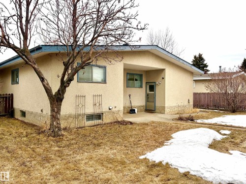 The property features a stucco exterior, a concrete patio area, and a fenced yard with a tree - 15208 92 Street, Edmonton, AB - Outdoor