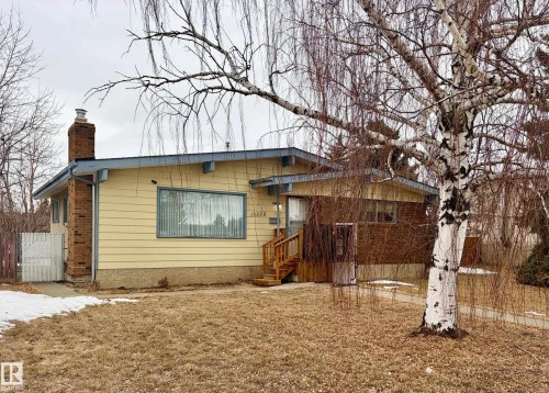 The property features a brick chimney, a wood front entry deck, and a front yard with a mature tree - 15208 92 Street, Edmonton, AB - Outdoor