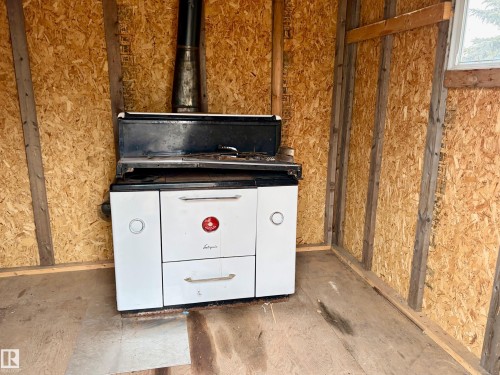 A white range with a black cooking surface is visible, featuring multiple knobs and handles, situated against a wall with exposed wood sheathing - 15208 92 Street, Edmonton, AB - Indoor