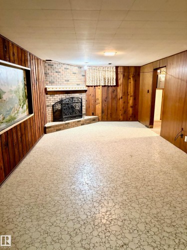 Living area featuring wood paneling, a brick fireplace with a hearth, and patterned flooring - 15208 92 Street, Edmonton, AB - Indoor Photo Showing Other Room