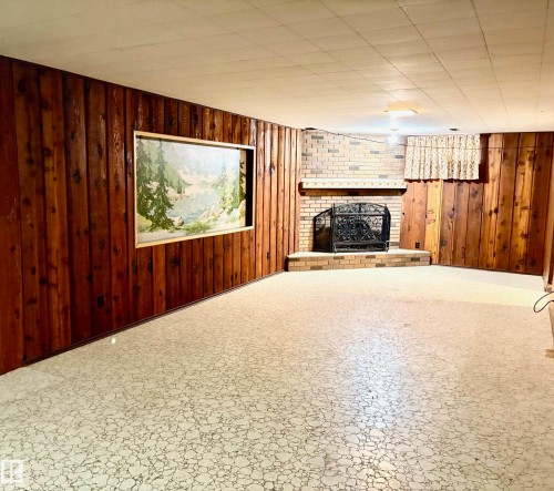 This inviting room features wood paneling, a brick fireplace with a decorative screen, and a dropped ceiling - 15208 92 Street, Edmonton, AB - Indoor With Fireplace