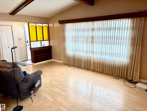 Living area featuring light-colored flooring, exposed ceiling beams, and a large window with privacy coverings - 15208 92 Street, Edmonton, AB - Indoor Photo Showing Other Room