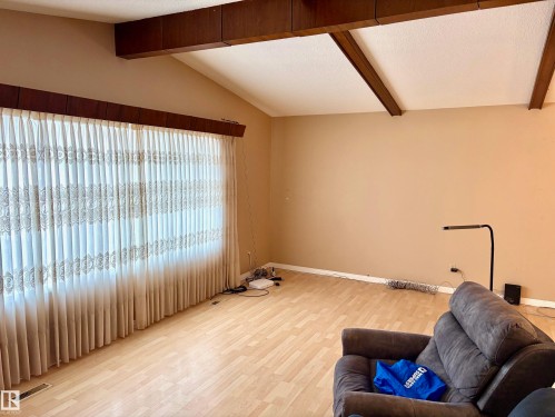 Spacious living area featuring light-toned flooring, a large window with privacy coverings, and exposed ceiling beams - 15208 92 Street, Edmonton, AB - Indoor Photo Showing Other Room