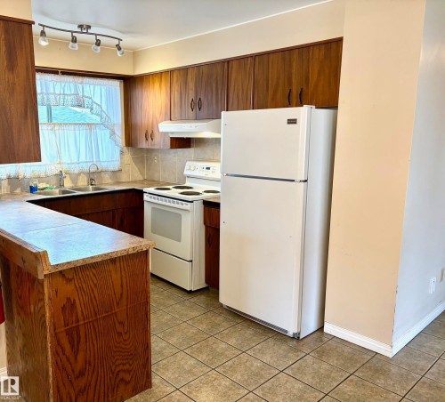 The kitchen features wood cabinetry, a double basin sink, and tile flooring - 15208 92 Street, Edmonton, AB - Indoor Photo Showing Kitchen With Double Sink
