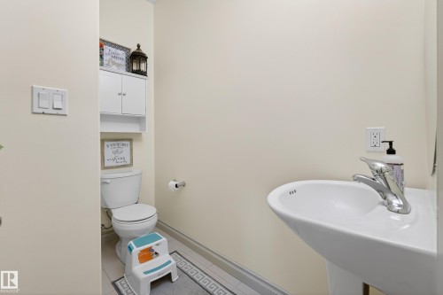 Pedestal sink with chrome faucet, toilet, and wall-mounted cabinetry - 7074 Cardinal Way, Edmonton, AB - Indoor Photo Showing Bathroom